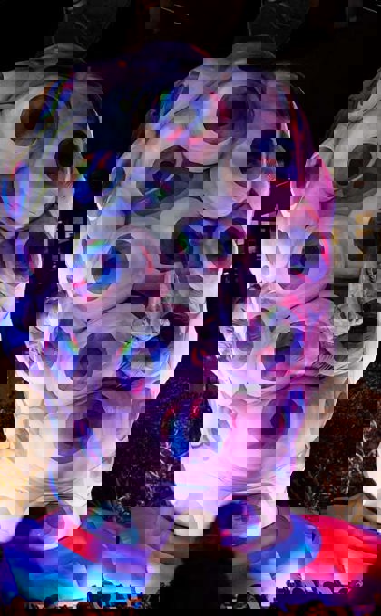 A large inflatable structure in the shape of a human head that is coloured purple and silver is covered in eyes looking outwards, with purple light all around.